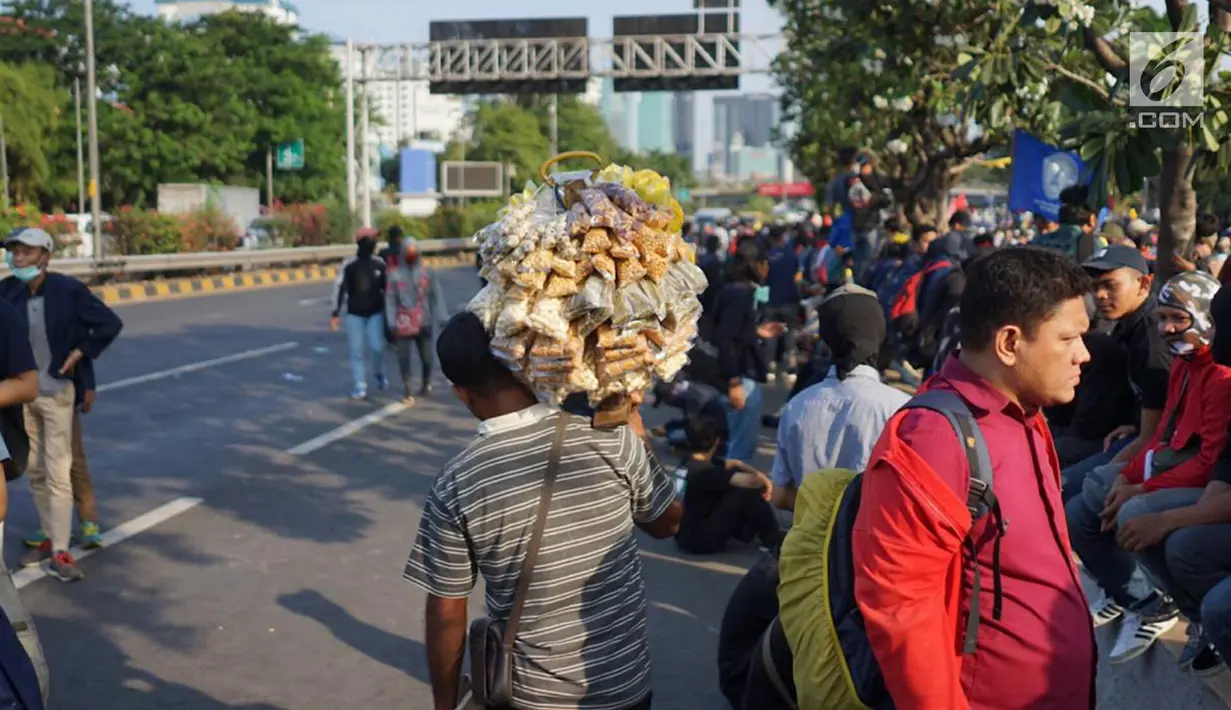 Seorang pedagang asongan menawarkan dagangannya di antara massa aksi di jalan tol dalam kota yang berada di depan Gedung DPR RI, Jakarta, Senin (30/9/2019). Adanya aksi unjuk rasa di sekitar lokasi dimanfaatkan para pedagang asongan untuk mencari rezeki. (Liputan6.com/Immanuel Antonius)