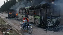 Pengendara motor melewati bangkai bus yang dibakar di dekat Idlib, Suriah, Minggu (18/12). Sedikitnya lima bus yang sedang dalam perjalanan mengevakuasi warga sipil korban perang di Aleppo timur dibakar sejumlah orang bersenjata. (REUTERS/Ammar Abdullah)