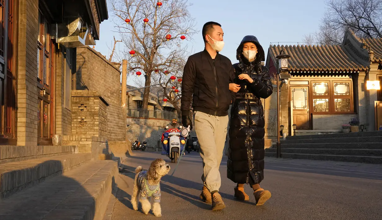 Warga yang mengenakan masker berjalan dengan anjing mereka di Beijing, China, Selasa (11/1/2022). Beijing dalam siaga tinggi menjelang Olimpiade Musim Dingin saat China mengunci kota ketiga di tempat lain akibat COVID-19. (AP Photo/Ng Han Guan)