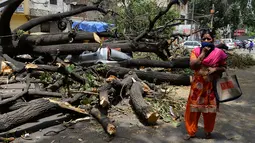 Seoarang wanita melintas di dekat mobil yang tertimpa pohon yang tumbang akibat  badai angin kencang di New Delhi, India (16/5). (AFP Photo/Sajjad Hussain)