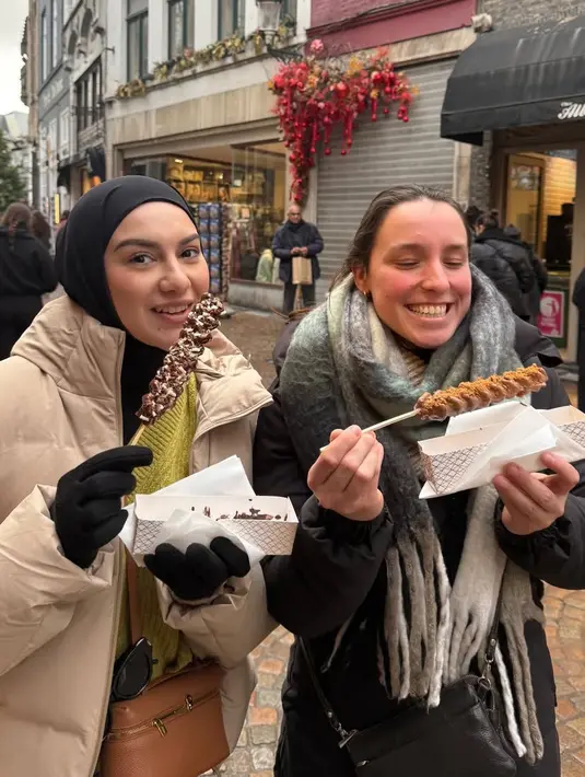 Menikmati kuliner Belgia, Irish pun mengenakan kerudung hitam dipadukan padding jaket warna beige serta sweater warna hijau lime. Tampak Irish pun mengenakan sarung tangan hitam. [@_irishbella_]