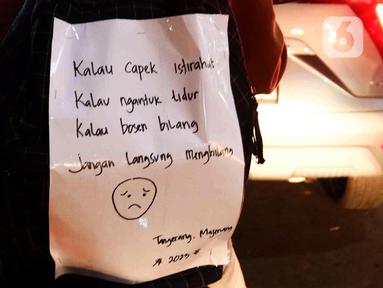 Sebuah kalimat menghiasi bagian belakang pemudik yang menggunakan sepeda motor di Jalan Raya Kalimalang, Bekasi, Jawa Barat, Rabu (19/4/2023) malam. (Liputan6.com/Herman Zakharia)
