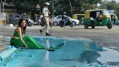 Seorang model berpakaian seperti putri duyung ambil bagian dalam seni instalasi seniman Baadal Nanjundawsamy di Bangalore, India, 13 Oktober 2107. Model itu terlihat bermain air yang telah dicampur cat air biru di tepi kubangan. (MANJUNATH KIRAN / AFP)