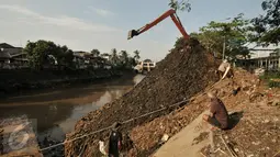 Warga melihat aktifitas pengerukan tumpukan sisa lumpur dan tanah yang menumpuk di pinggir kali Ciliwung, Jakarta, Kamis (28/7). Dinas Tata Air DKI Jakarta bersihkan tumpukan tanah dan lumpur sisa pengerukan kali Ciliwung. (Liputan6.com/Yoppy Renato)