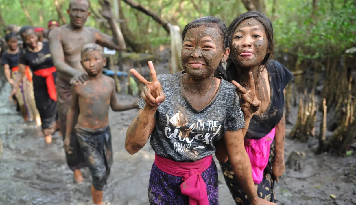 Dua remaja berpose dengan badan penuh lumpur saat mengikuti Mebuug-buugan di desa Kedonganan, Bali (18/3). Tujuan dari tradisi ini tak lain untuk menetralisir dan membersihkan dari hal-hal atau sifat buruk. (AFP/Sony Tumbelaka)