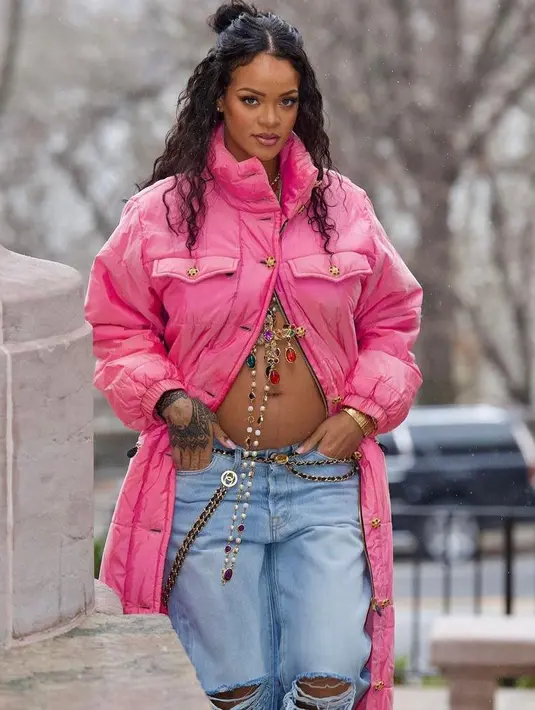 Rihanna menunjukkan baby bump-nya dengan mengenakan jaket merah muda cerah yang tidak dikancing di bagian bawah untuk memamerkan perutnya, yang dihiasi dengan salib emas dan permata. (Instagram/badgalriri).
