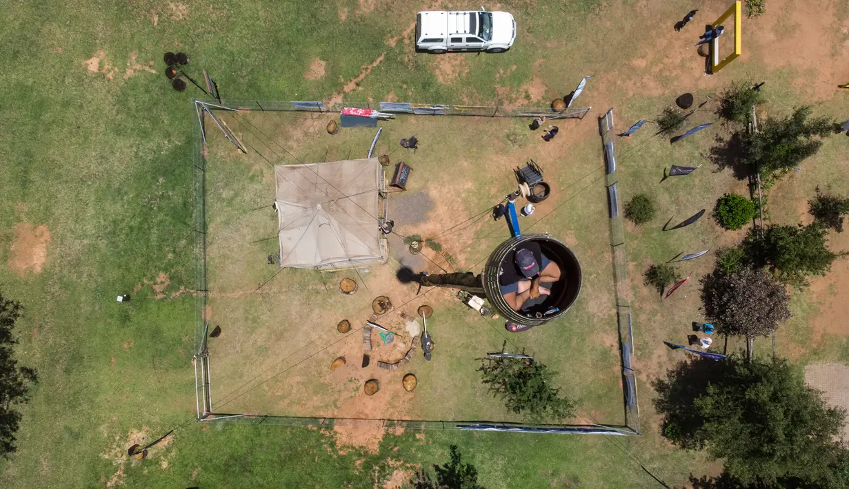 Pandangan aerial memperlihatkan Vernon Kruger, 52, duduk dalam tong di atas tiang berketinggian 25 meter di Dullstroom, 16 Januari 2020. Di dalam tong itu, ada pipa kecil untuk menyalurkan pembuangan hajat Kruger serta makanan yang diantarkan ke atas oleh tim dengan keranjang. (ANTOINE DEMAISON/AFP)