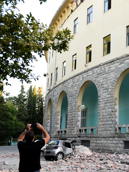 Seorang pria mengabadikan gedung yang runtuh sai gempa berkekuatan 5,6 magnitudo mengguncang Tirana, Albania (21/9/2019). Efek dari gempa bumi tersebut mengakibatkan puluhan bangunan hancur serta memicu pemadaman listrik di ibu kota Tirana. (AFP Photo/Gent Shkullaku)