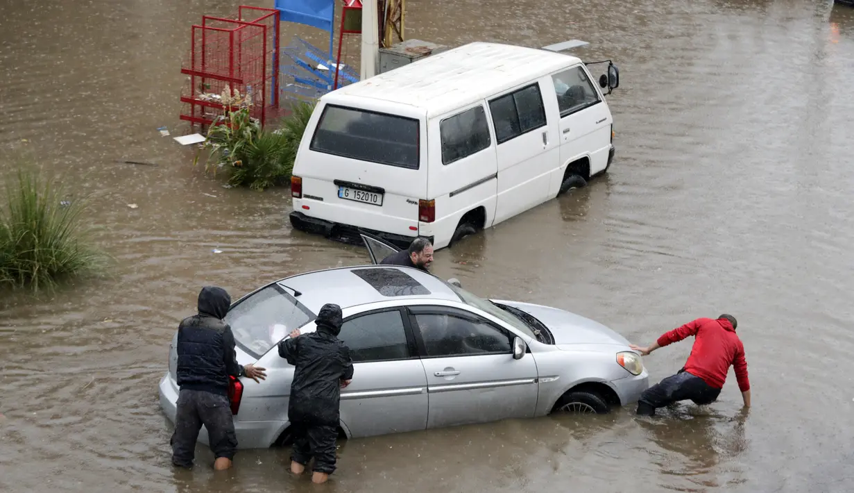 Warga mendorong sebuah mobil yang mogok di jalan banjir akibat hujan deras di Beirut, Lebanon (9/12/2019). Hujan deras membuat sejumlah rumah dan kendaraan di Lebanon terendam banjir dan melumpuhkan daerah-daerah dari ibukota Beirut, Lebanon. (AFP Photo/Anwar Amro)