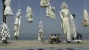 Sejumlah wanita duduk dekat puluhan gaun pengantin yang digantung di tepi pantai Beirut, Sabtu (22/4). Sekitar 30 gaun pengantin menggambarkan kondisi mencekam, lusuh dan berwarna pudar sebagai bentuk protes UU Pemerkosaan di Lebanon. (PATRICK BAZ/AFP)