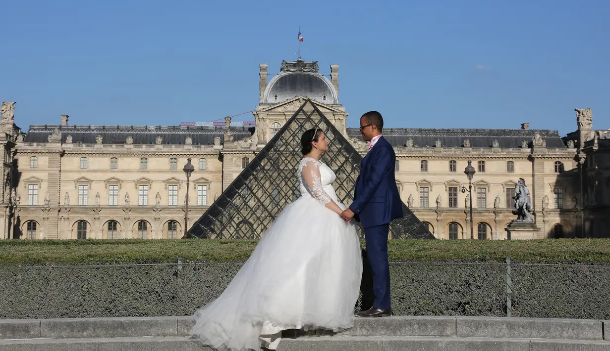Sepasang calon pengantin melakukan foto prewedding dengan latar belakang Pyramide de Louvre di Paris, 9 Juli 2017. Bukan cuma menara Eiffel yang sudah amat terkenal itu, ibukota Perancis ini juga punya Piramida Louvre. (AFP PHOTO / LUDOVIC MARIN)