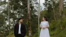 Salah satu foto memperlihatkan Frans dan Indah berada di hutan dengan pepohonan tinggi yang menjulang. Indah tampil anggun dalam gaun putih beraksen renda yang memancarkan kesan klasik, sedangkan Frans mengenakan setelan jas hitam dengan kemeja putih, tampil rapi dan elegan. Komposisi kayu besar di latar depan menambah elemen artistik sekaligus menciptakan kesan alami yang tenang. (Liputan6.com/IG/@fransfaisal_)