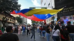 Mereka meneriakkan slogan anti-imperialisme dan menyatakan bahwa Venezuela bukan negara yang akan menyerah. Tampak dalam foto, seorang pendukung mantan Presiden Venezuela, Nicolas Maduro, membawa bendera nasional saat mengikuti aksi unjuk rasa di Caracas pada Minggu 4 Januari 2026. (Juan BARRETO/AFP)