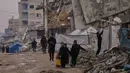 Kepala Badan Perserikatan Bangsa Bangsa (PBB) untuk Pengungsi Palestina (UNRWA), Philippe Lazzarini mengatakan selama berbulan-bulan konflik, ratusan ribu warga terpaksa tinggal di reruntuhan bangunan, tempat perlindungan darurat, serta tenda-tenda darurat yang tidak mampu melindungi dari hujan lebat dan angin kencang. Tampak dalam foto, warga Palestina berjalan di sepanjang jalan yang dikelilingi bangunan-bangunan yang hancur akibat serangan udara dan darat Israel di lingkungan Sheikh Radwan, Kota Gaza, Selasa, 30 Desember 2025. (AP Photo/Abdel Kareem Hana)