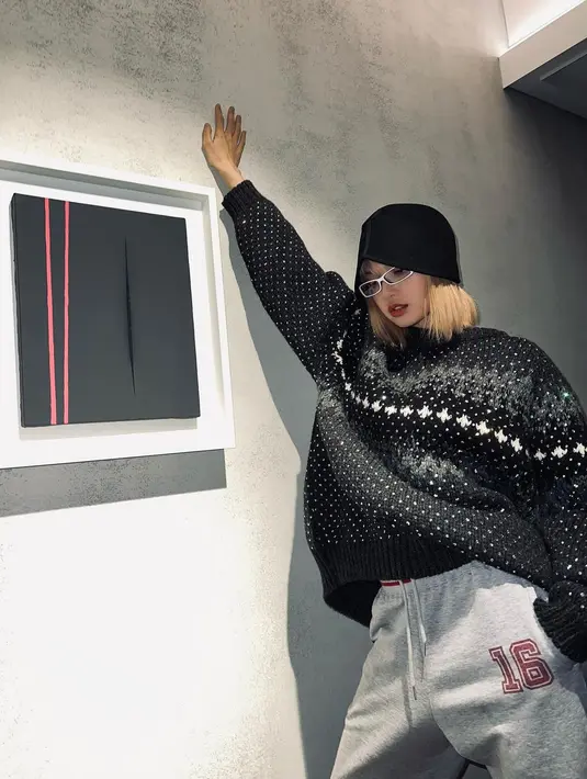 Berpose dalam outfit bernuansa kasual, Lisa terlihat mengenakan sweater bermotif totol hitam-putih. Ia padukan dengan jogger pants abu-abu, kacamata berbingkai putih, dan cloche hat hitam. Foto: Instagram.