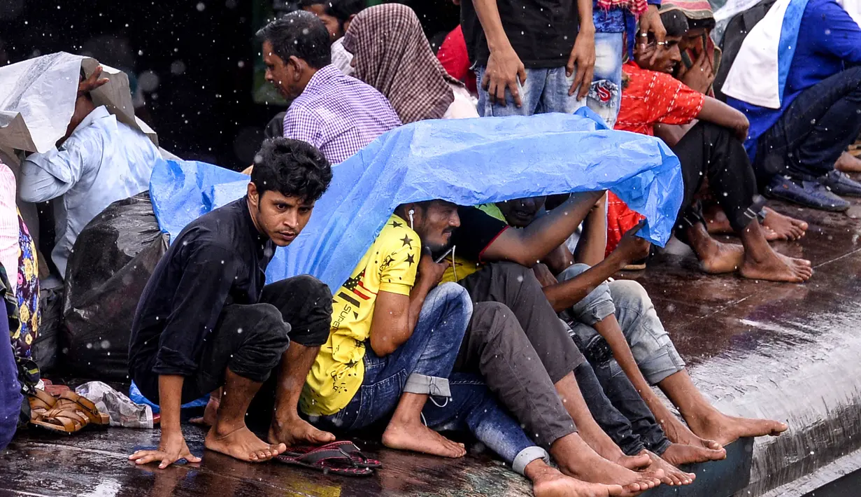 Warga Bangladesh melindungi diri mereka dari hujan saat duduk di atas atap kereta untuk menuju kampung halaman di Dhaka pada 4 Juni 2019. Sebagaimana terjadi di Indonesia, masyarakat Bangladesh pun memiliki tradisi mudik saat Idul Fitri, namun agak membahayakan keselamatan. (MUNIR UZ ZAMAN/AFP)