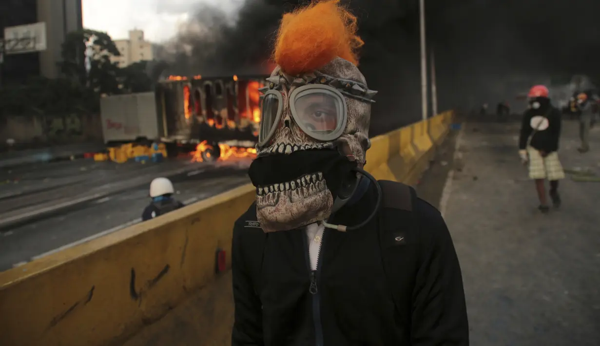 Demonstran anti-pemerintah di Venezuela mengenakan masker saat menggelar aksi di Caracas, Venezuela, Sabtu (26/5). Gelombang protes disebabkan oleh keputusan Mahkamah Agung untuk mengambil fungsi parlemen negara yang dikuasai oposisi. (AP Photo)  