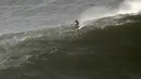 Seorang peselancar mengendarai papan hidrofoil menuruni gelombang selama sesi selancar derek di Praia do Norte atau Pantai Utara di Nazare, Portugal, Kamis (29/10/2020). (AP Photo/Pedro Rocha)
