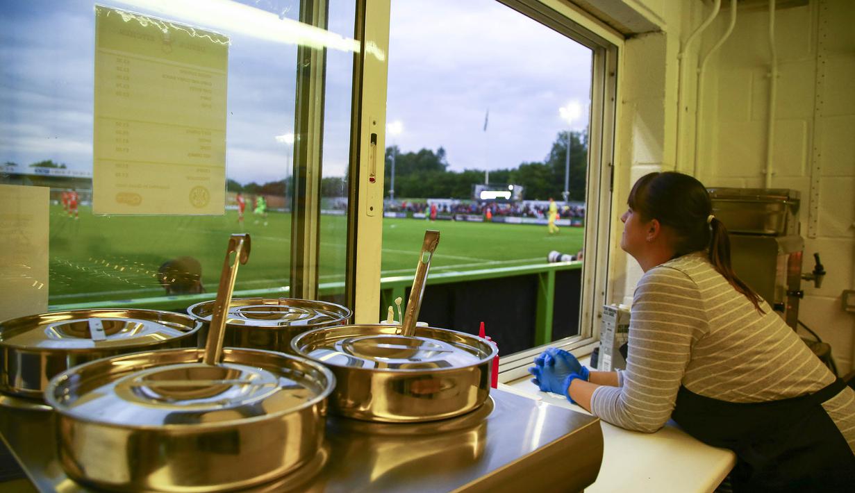 Seorang petugas menyaksikan laga Piala Liga antara Forest Green Rovers melawan MK Dons dari dapur di Stadion New Lawn, Nailsworth, Selasa (8/8/2017). FGB merupakan klub sepak bola yang mengedepankan hidup sehat dan ramah lingkungan. (AFP/Geoff Caddick)