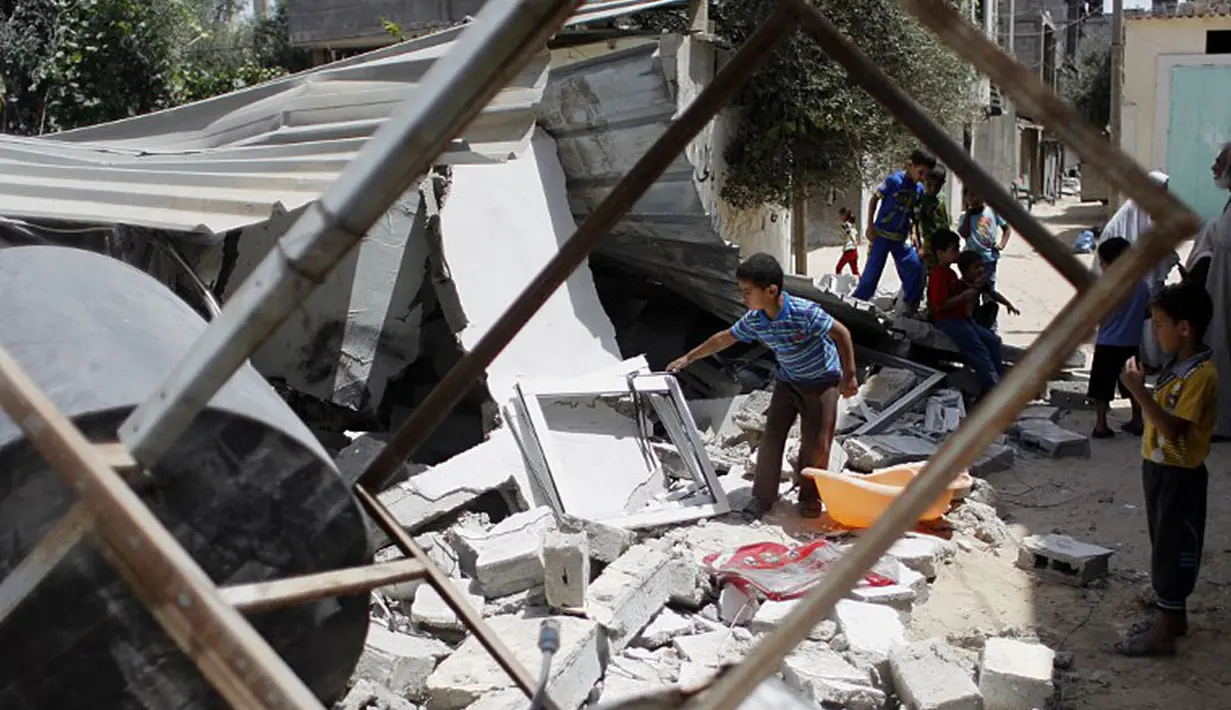 Beberapa anak mengais puing mencari barang berharga di atas reruntuhan bangunan yang hancur di kota Rafah, selatan jalur Gaza, Palestina, (12/7/2014). (AFP PHOTO/Said Khatib)