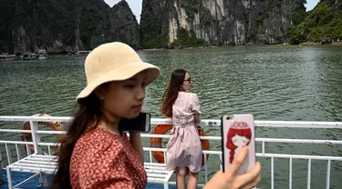 Wisatawan domestik berpose untuk foto di atas kapal di tengah Ha Long Bay, Quang Ninh, Vietnam, (16/5/2020). Sempat terpukul akibat pandemi virus corona Covid-19, pariwisata Vietnam kembali menggeliat setelah otoritas setempat melonggarkan pembatasan perjalanan. (AFP/Manan Vatsyayana)