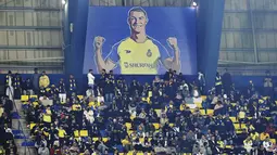 Penggemar Al Nassr duduk di bawah papan reklame raksasa yang memperlihatkan Cristiano Ronaldo selama pertandingan Liga Pro Saudi antara Al Nassr dan Al Ettifaq di Stadion Mrsool Park di Riyadh, Arab Saudi, Minggu (22/1/2023). Meski Ronaldo menjadi kapten tim gagal mencetak gol dalam debutnya. (AP Photo)