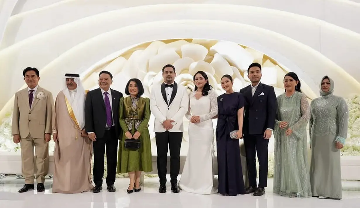 Saat menyambut para tamu, Kenia masih mengenakan gaun panjang putih. Namun, ia lebih memilih rambut panjangnya terurai. Sementara itu, suaminya mengenakan tuxedo putih kerah hitam senada dengan dasi kupu-kupu dan celana panjangnya.  [@profottohasibuan]