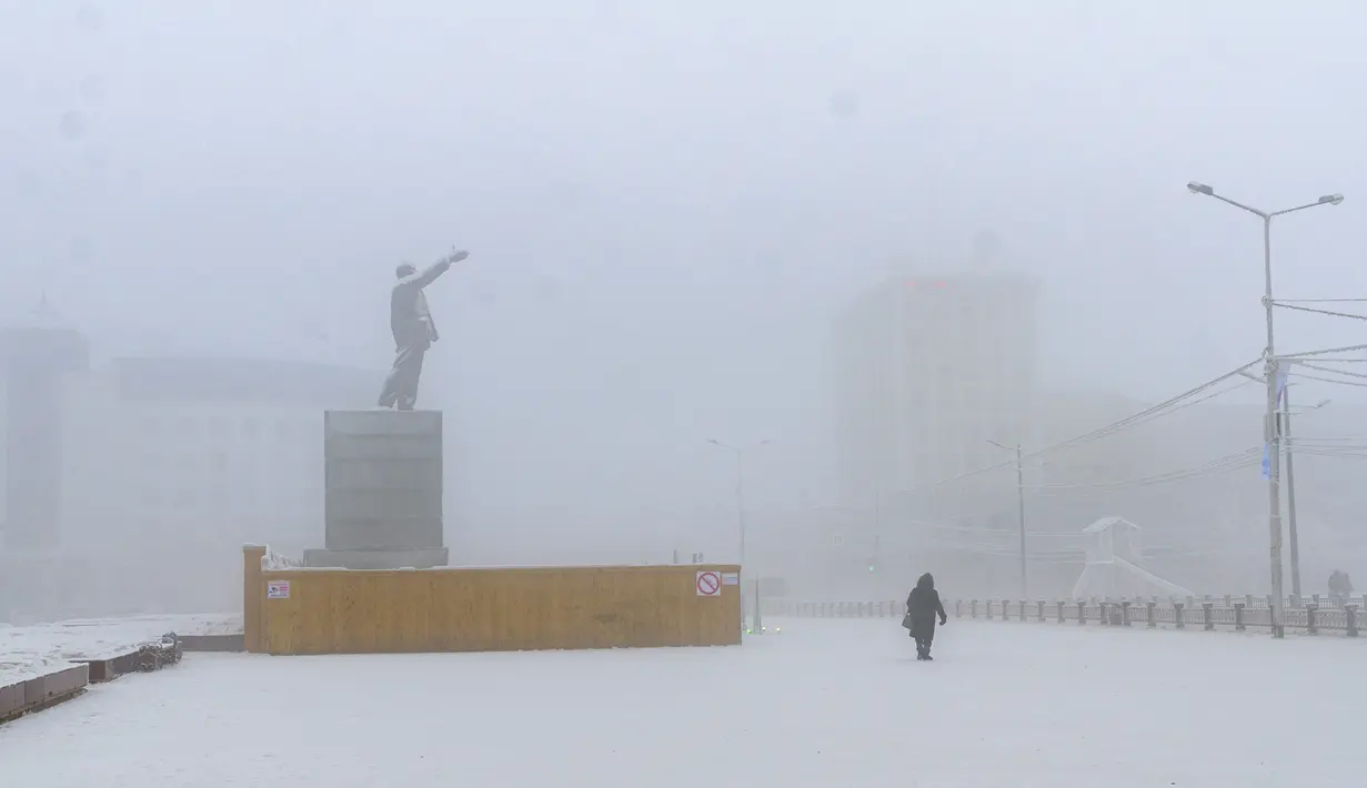 Seorang perempuan berjalan melewati patung pendiri Uni Soviet Vladimir Lenin saat suhu turun hingga sekitar minus 50 derajat Celcius (-58 derajat Fahrenheit) di Yakutsk, Rusia, Sabtu (16/1/2021).  Yakutsk atau Yakutia tersohor sebagai kota terdingin di dunia. (AP Photo/Ajar Warlamov)
