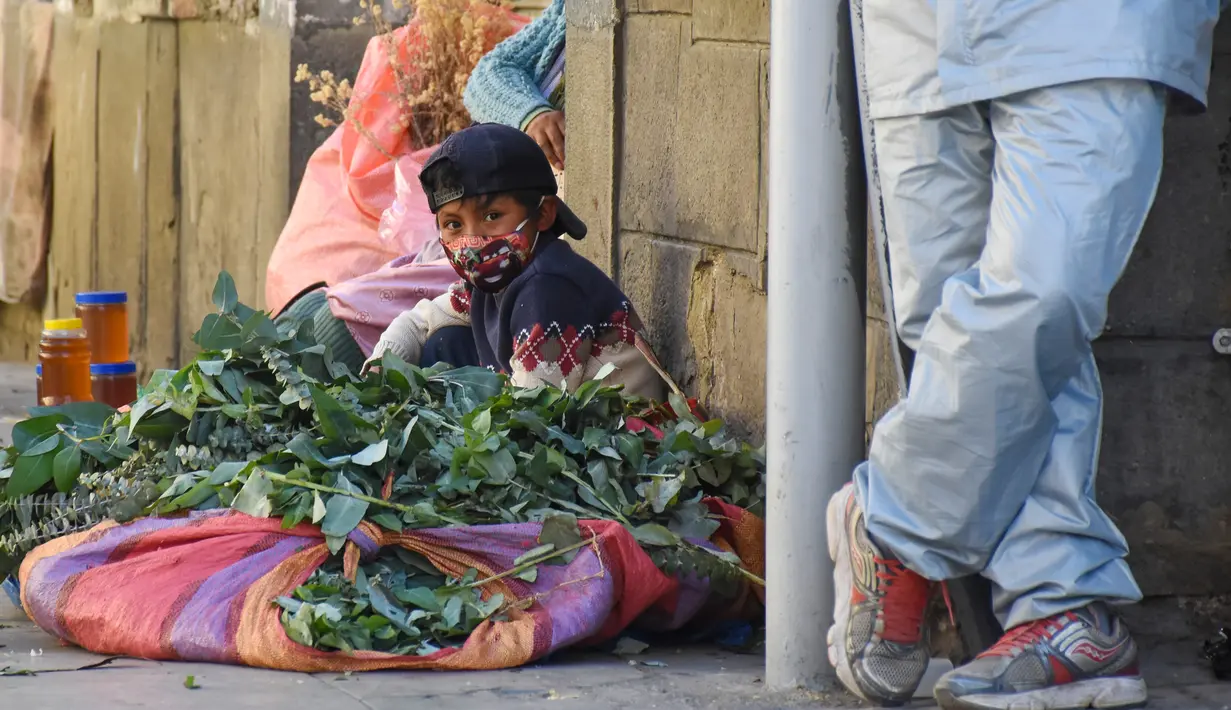 Seorang anak terlihat di mana ibunya menjual ramuan obat tradisional untuk pengobatan penyakit pernapasan di trotoar di Cochabamba, Bolivia pada 25 Juli 2020. Kasus infeksi virus corona dan kematian akibat COVID-19 semakin meningkat di negara Amerika Selatan tersebut. (AP Photo/Dico Solis)