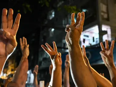 Orang-orang memberi hormat tiga jari setelah seruan untuk protes keluar di media sosial di Yangon, Myanmar, 3 Februari 2021. Kudeta militer Myanmar terus memicu protes warga dengan membunyikan klakson mobil, menyalakan lampu ponsel, dan memukul-mukul panci. (STR/AFP)