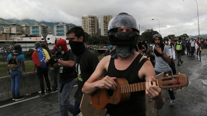 Seorang demonstran anti-pemerintah memakai pelindung wajah memainkan gitar kecil saat demonstrasi melawan Presiden Nicolas Maduro di sepanjang jalan raya di Caracas, Venezuela,(19/6). (AP Photo / Fernando Llano)