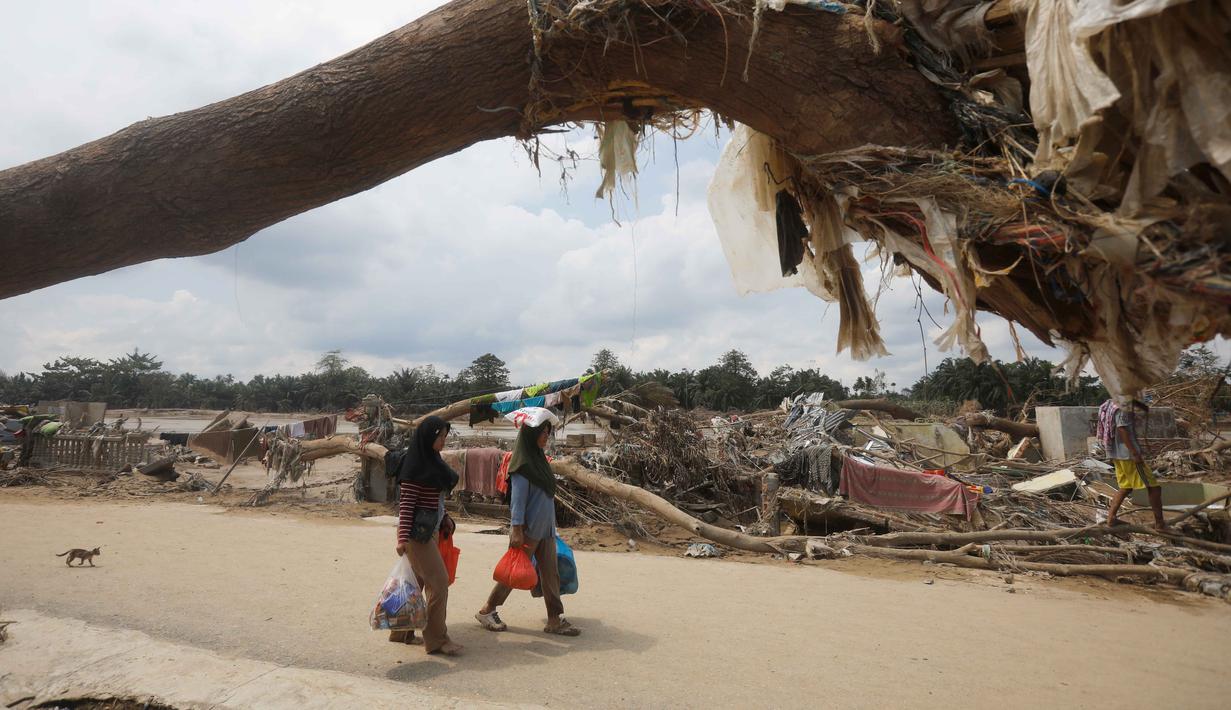 Kondisi kesehatan warga juga semakin terancam. Tampak dalam foto, para penyintas berjalan melewati puing-puing di area yang hancur akibat banjir bandang di Aceh Tamiang, Pulau Sumatra, Jumat 5 Desember 2025. (AP Photo/Binsar Bakkara)