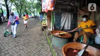 Warga bejalan kaki melewati pembuat dodol Betawi di Setu Babakan, Jagakarsa, Jakarta Selatan, Minggu (4/4/2021). Setu Babakan kembali dibuka untuk umum pada 27 Maret 2021 dengan menerapkan protokol kesehatan. (merdeka.com/Arie Basuki)