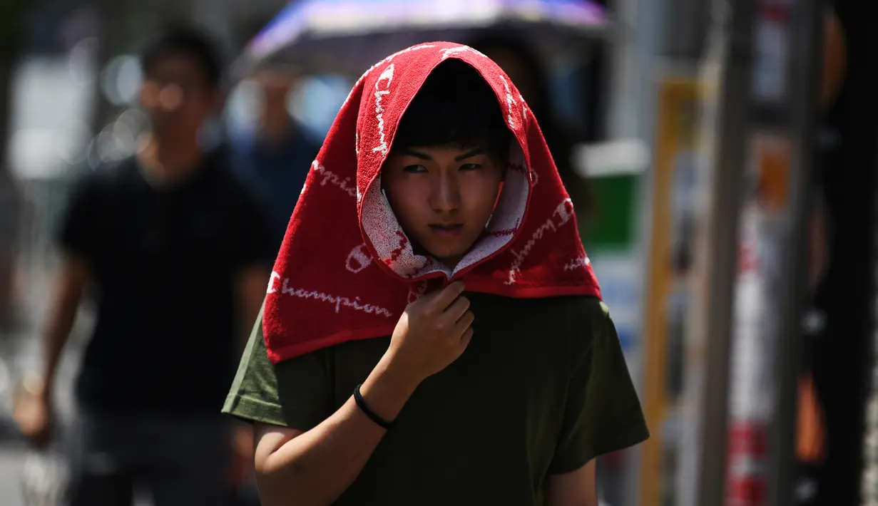 Seorang pria melindungi dirinya dari sinar matahari dengan handuk yang menutupi kepala selama gelombang panas di distrik Shin-Okubo Tokyo pada Minggu (4/8/2019). Setelah menyerang beberapa wilayah di Eropa, suhu tinggi juga terjadi di Jepang. (Charly TRIBALLEAU / AFP)