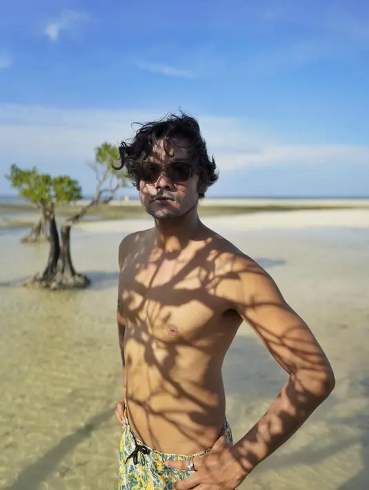Menikmati pemandangan di pantai, Dwi Sasono memilih bergaya topless dengan kacamata hitam. Tubuh atletisnya membuat ia terlihat makin macho. (Liputan6.com/IG/@dwisasono)