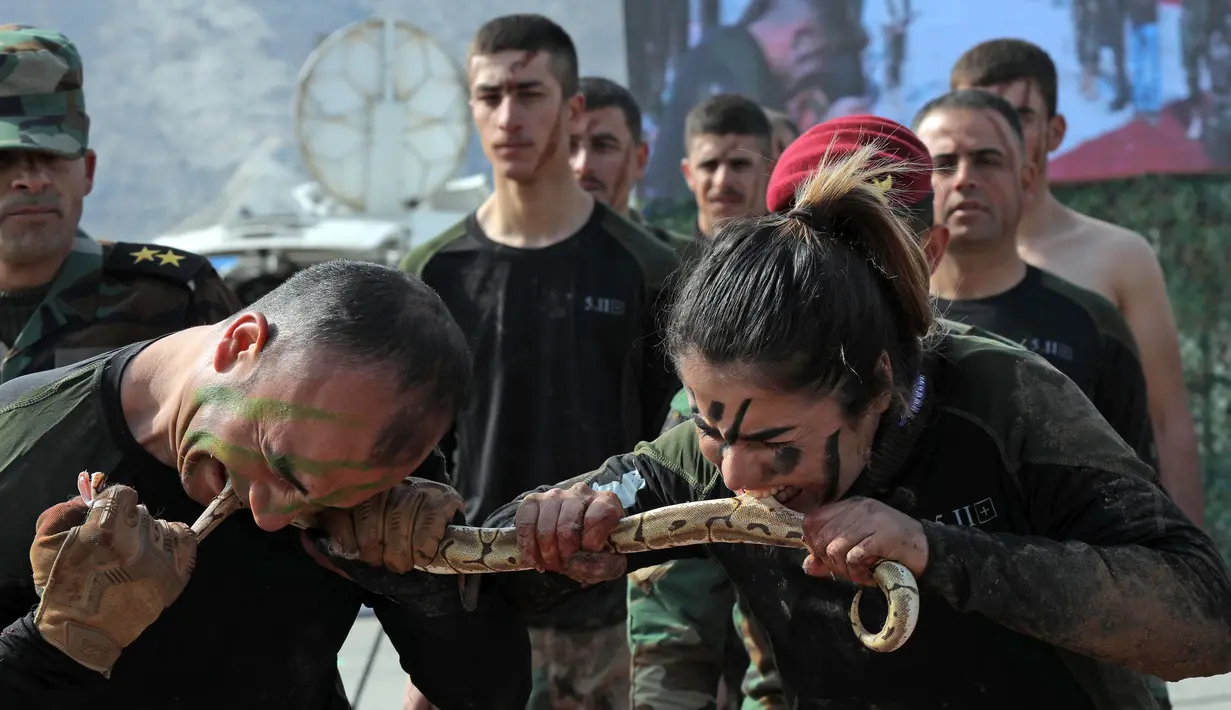 Pasukan perempuan Peshmerga bersama seorang pria menggigit ular saat berlatihan dalam upacara kelulusan di Kota Soran, Irak, Rabu (12/2/2020). Latihan militer pasukan bersenjata Kurdi tersebut dilakukan sekitar 100 kilometer timur laut ibu kota otonomi wilayah Kurdi di Irak, Arbil. (SAFIN HAMED/AFP)