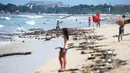Turis berjalan melintasi puing-puing dan sampah di pesisir Pantai Kuta, Bali, Minggu (9/12). Kawasan pantai Kuta kembali dipenuhi oleh sampah hanyut terbawa oleh gelombang. (SONNY TUMBELAKA / AFP)