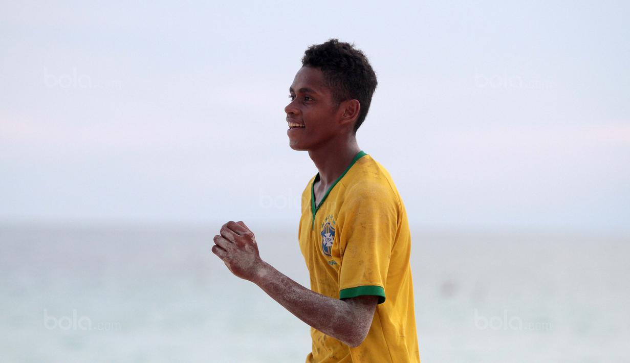 Seorang pemuda menggunakan jersey Brasil saat bermain bola dekat pantai di Desa Matwaer, Kei Kecil, Maluku (25/12/2017). Bermain bola di pasir menjadi daya tarik tersendiri bagi anak-anak dan pemuda desa. (Bola.com/Nick Hanoatubun)