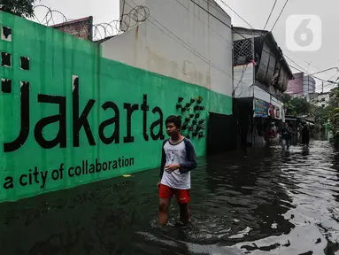 Seorang remaja melintasi banjir yang merendam lingkungan rumah tempat tinggal mereka di kawasan kecamatan Kebayoran Baru, Jakarta, Senin (25/01/2021). Hujan deras yang mengguyur Jakarta hari ini, Senin (25/1) menyebabkan terjadinya banjir di kawasan permukiman tersebut. (Liputan6.com/Johan Tallo)
