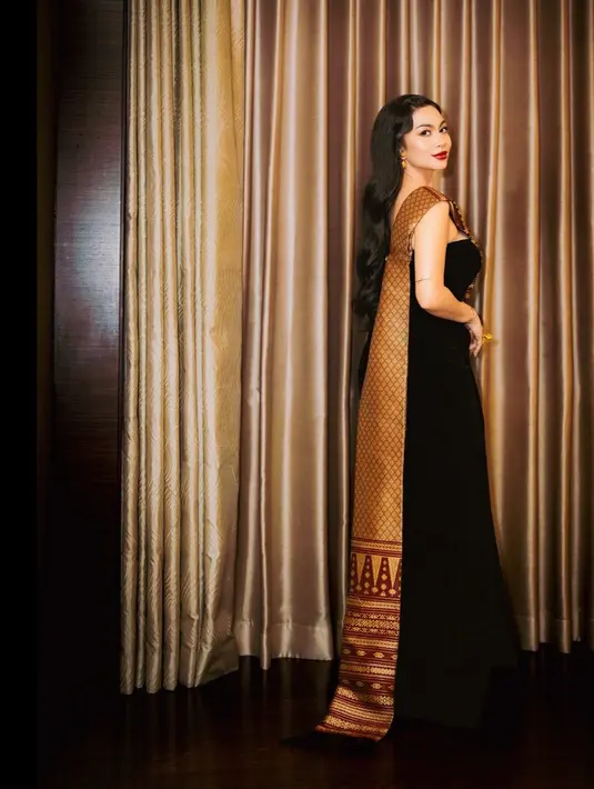 Kain ulos berwarna merah dengan motif emas dan aksen one shoulder hingga belakang dress [@arieltatum]