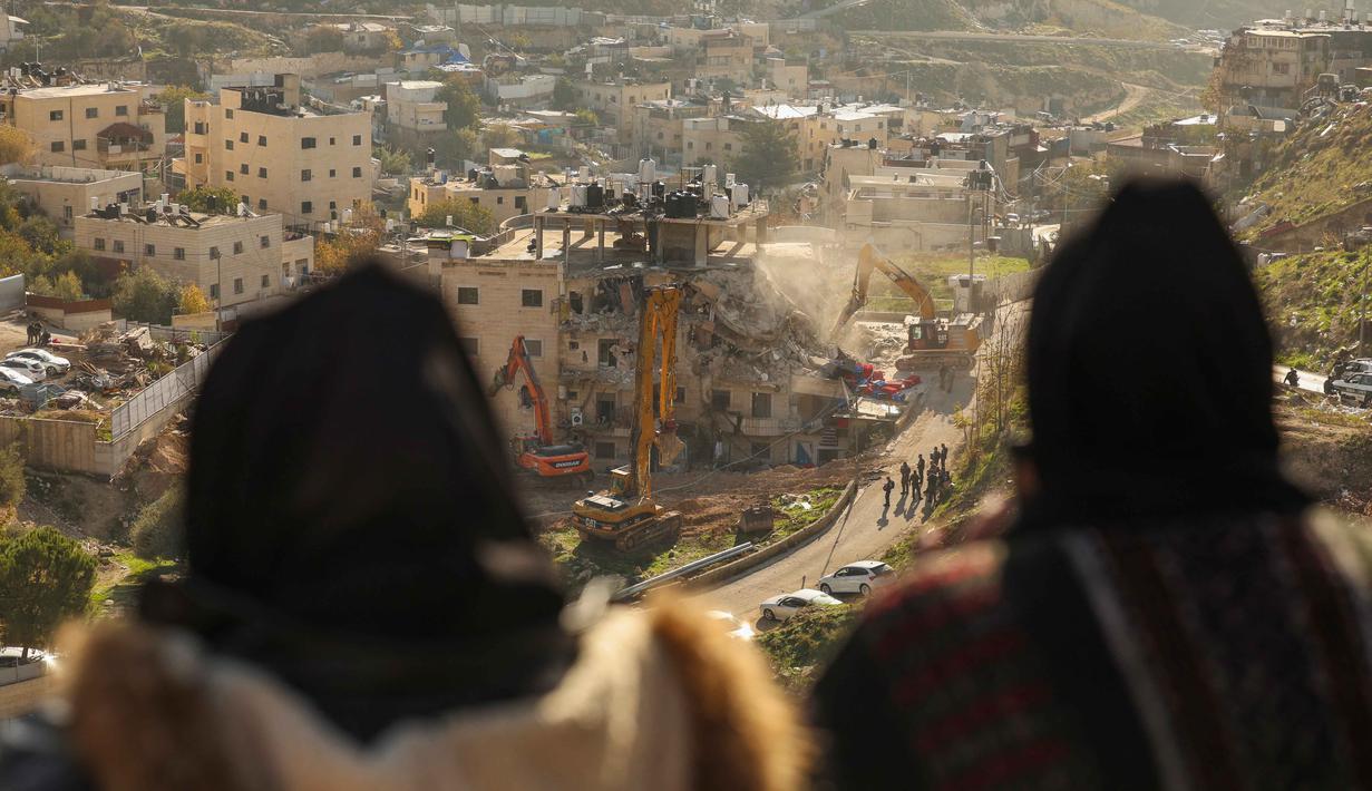 Para perempuan Palestina menyaksikan pasukan Israel yang menggunakan ekskavator merobohkan sebuah bangunan yang dibangun tanpa izin di lingkungan Wadi Qaddum, Yerusalem timur, pada Senin 22 Desember 2025. Ratusan warga Palestina terusir saat buldoser-buldoser Israel meratakan sebuah bangunan tempat tinggal empat lantai di wilayah Yerusalem Timur. (Ahmad GHARABLI/AFP)