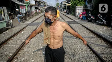 Seorang pria berjemur di bantaran rel di kawasan pemukiman padat Pejompongan, Jakarta, Selasa (6/7/2021). Berjemur diri di bawah matahari di antara pukul 08.00-11.00 WIB merupakan salah satu upaya yang paling sederhana untuk menjaga kesehatan selama wabah virus COVID-19. (Liputan6.com/Faizal Fanani)