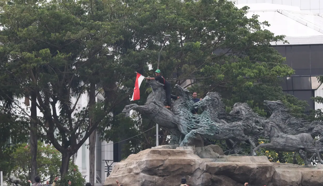 Massa aksi demo tolak omnibus law UU Cipta Kerja naik ke atas patung arjuna wiwaha membawa bendera merah putih di Jalan Medan Merdeka Barat, Jakarta Pusat, Selasa (20/10/2020). Mereka sempat mengibarkan bendera selama kurang lebih lima menit di atas patung. (Liputan6.com/Herman Zakharia)