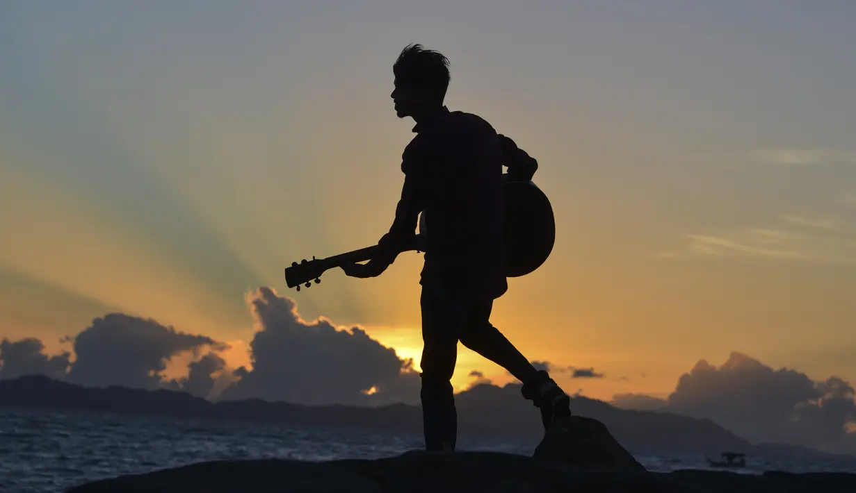 Seorang pria memainkan gitar saat matahari terbenam atau sunset di pantai Banda Aceh pada 28 Juni 2019. Pemandangan makin sempurna saat matahari tenggelam hingga alam berubah semakin remang dan romantis. (Photo by CHAIDEER MAHYUDDIN / AFP)