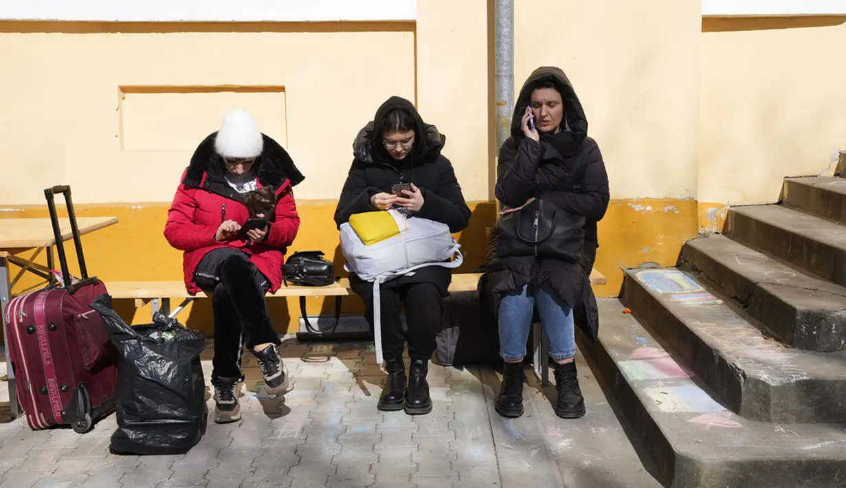 Tiga wanita memeriksa ponsel mereka saat beristirahat di pusat penerimaan pengungsi yang melarikan diri dari Ukraina di Beregsurany, Hungaria, 8 Maret 2022. PBB mengatakan, serangan gencar Rusia telah memaksa lebih dari 2 juta orang meninggalkan Ukraina. (AP Photo/Darko Vojinovic)