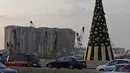 Kendaraan melintas di samping pohon Natal dengan daftar nama korban yang tewas dalam insiden ledakan di Pelabuhan Beirut terlihat di dekat silo gandum yang rusak di Beirut, Lebanon (22/12/2020). Ledakan juga menyebabkan 300.000 orang kehilangan tempat tinggal. (Xinhua/Bilal Jawich)