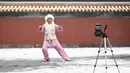 Seorang wanita merekam dirinya melakukan tai chi ketika salju turun di sebuah taman di Beijing (16/12/2019). Salju yang melanda Beijing Senin pagi membuat penerbangan dibatalkan dan rute bus disesuaikan. (AFP Photo/Wang Zhao)