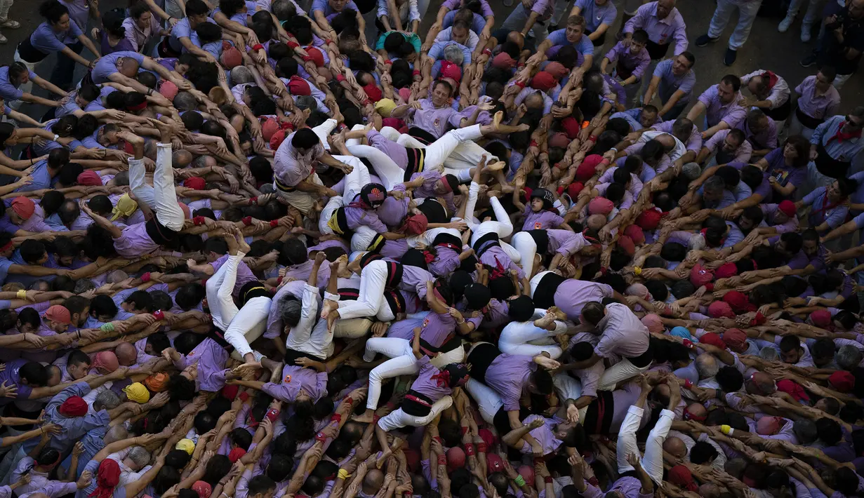 Anggota "Jove de Tarragona" jatuh saat mereka mencoba menyelesaikan menara manusia mereka selama Kompetisi Menara Manusia ke-28 di Tarragona, Spanyol, Minggu (2/10/2022). Mereka yang bagian bawah saling mengunci tangan mereka agar bisa kuat dinaiki orang yang menjadi menara hingga 10 tingkat. (AP Photo/Joan Mateu Parra)
