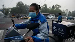 Seorang pekerja pengiriman mengenakan masker pelindung untuk menghindari polusi udara buruk di Beijing (22/10). (AFP Photo/Nicolas Asfaouri)