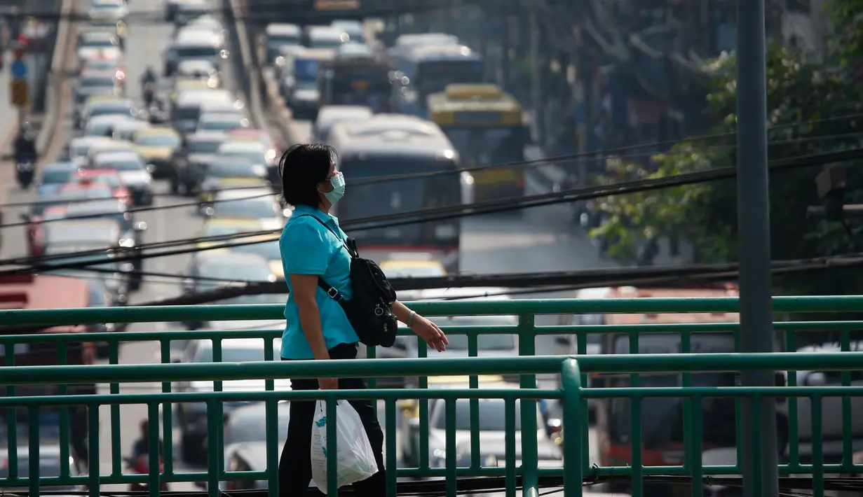 Pejalan kaki memakai masker pelindung saat melintasi jembatan layang selama kabut asap menyelimuti Bangkok (14/1). Tingkat kabut asap yang sangat tinggi diperburuk oleh pola cuaca yang meningkatkan kewaspadaan di seluruh Asia. (AP Photo/Sakchai Lalit)